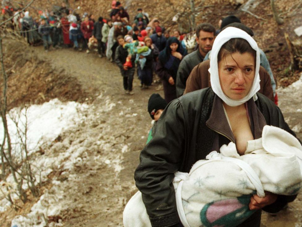 File photo of an ethnic Albanian woman feeding her baby as she and another 2,000 refugees walk up a muddy dirt track after they were allowed to enter Macedonia