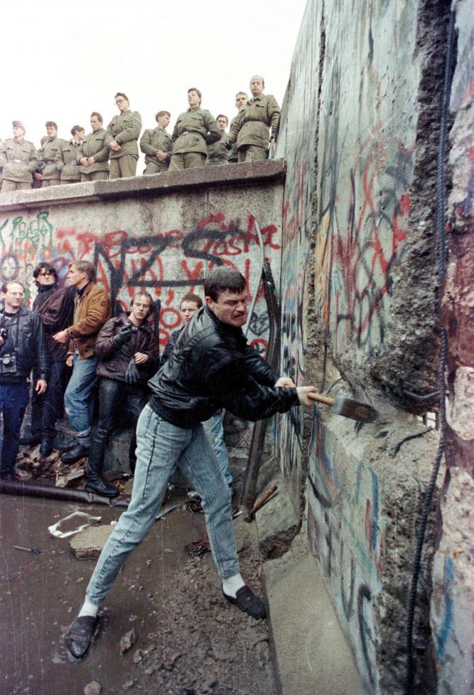 File photo of a demonstrator pounding away at the Berlin Wall as East Berlin border guards look on from above the Brandenburg Gate