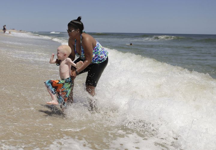 Global Medical Relief Fund assistant Monica Watson, right, helps Baraka Lusambo, 5, dart away from an approaching wave in Long Beach Island, N.J. on Wednesday, July 22, 2015. One out of every 1,400 citizens in Tanzania has albinism. Baraka was attacked and dismembered in the belief that their body parts will bring wealth. (AP Photo/Julie Jacobson)