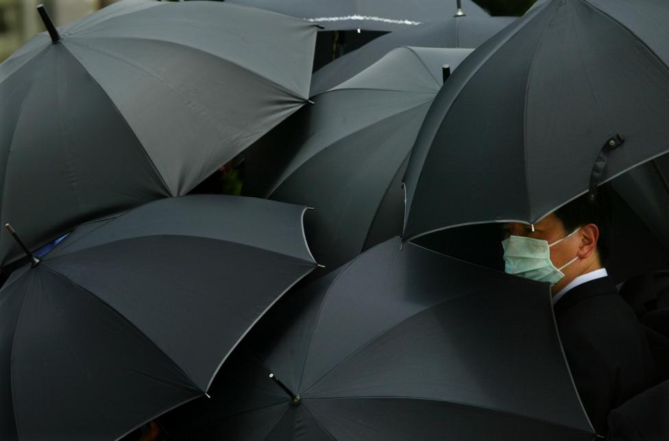 File photo of a mourner wearing a mask to ward off SARS hiding under an umbrella during the funeral of Dr Tse-Yuen-man in Hong Kong
