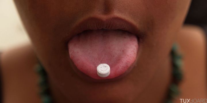 Girl with an ecstasy tablet on her tongue, smiley faced pill, UK 2004